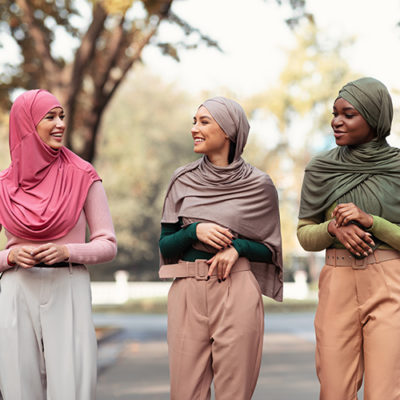 Three Modern Muslim Young Women In Hijab Headscarf Walking In Park Outdoors. Cheerful Islamic Students Ladies Talking Enjoying Walk Outside. Female Frienship, Fashion Concept